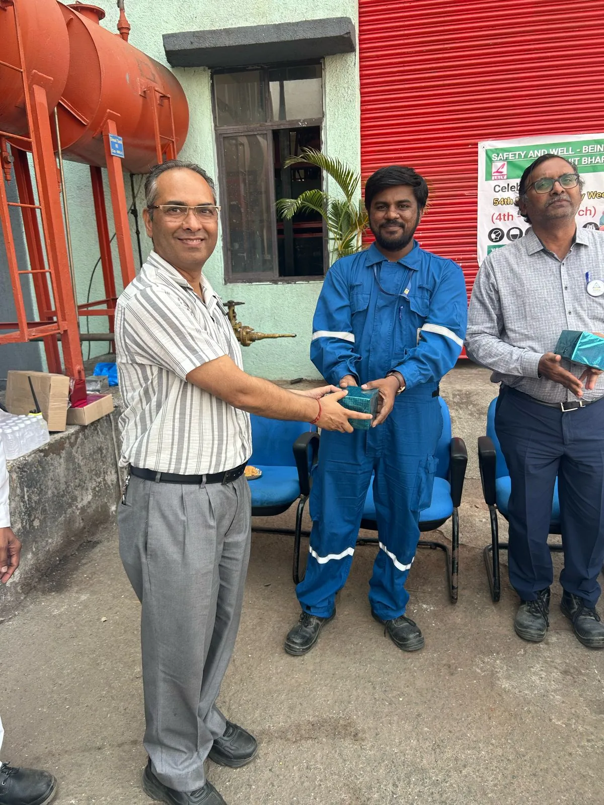 A worker in blue coveralls and two other participants stand together holding a presentation item at the terminal.