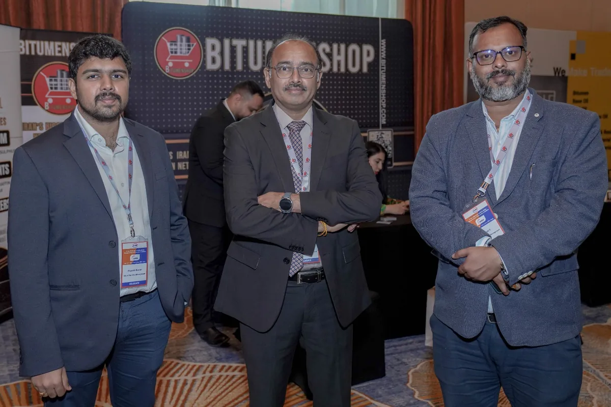 Three industry event delegates stand for a photograph beside a Bitumenshop display.