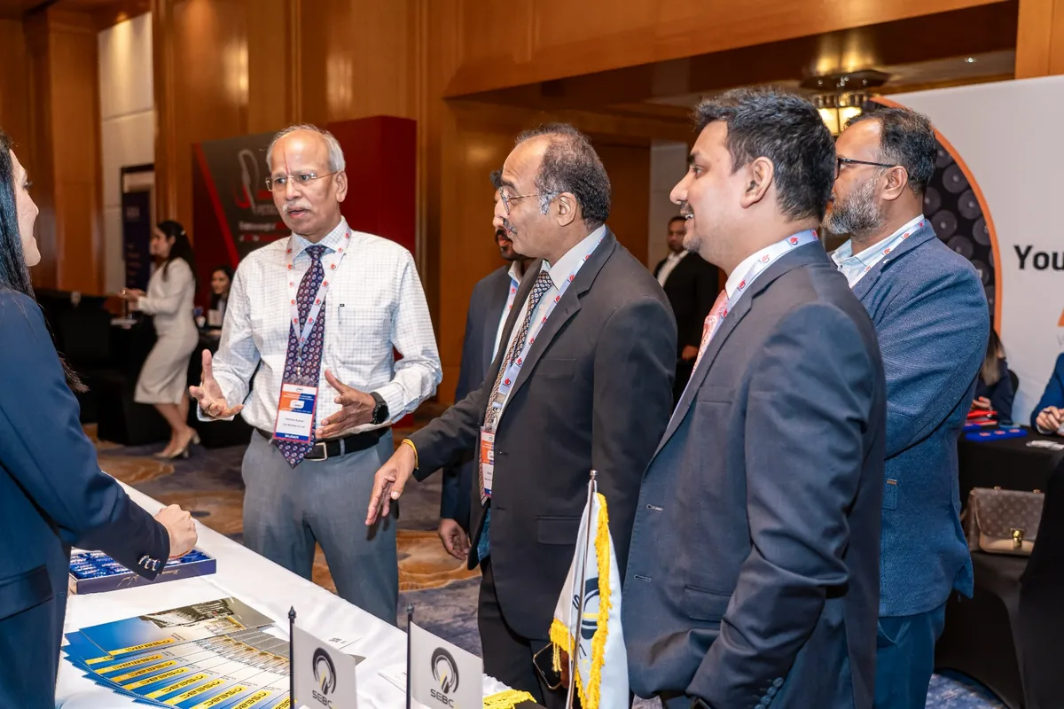 Delegates converse beside an exhibition table in a wood-panelled conference venue.