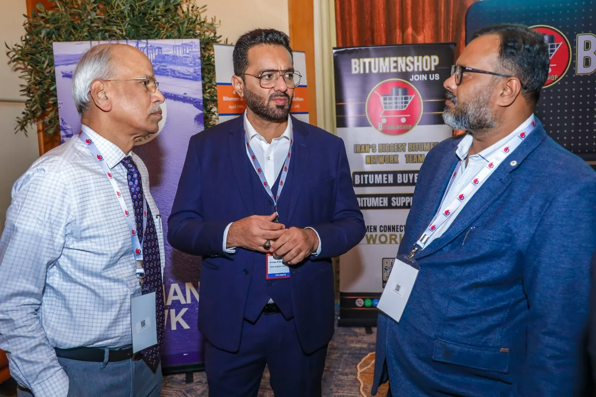 Three delegates discuss an exhibit in front of a Bitumenshop display.