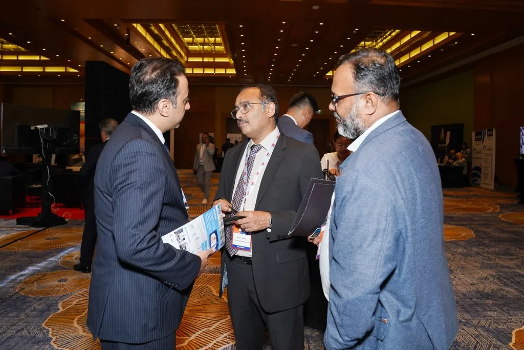 Three suited delegates discuss printed materials while standing in a conference hall.