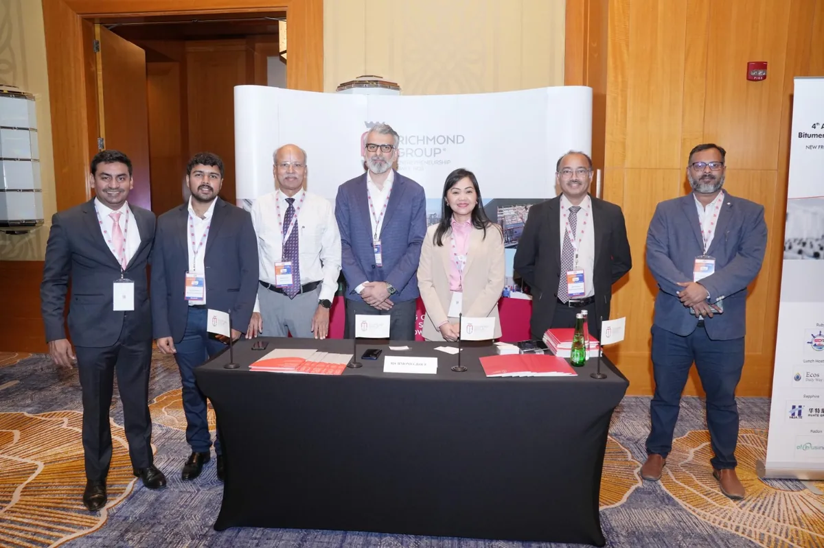 Seven delegates gather for a photograph behind an exhibition table and a white event backdrop.