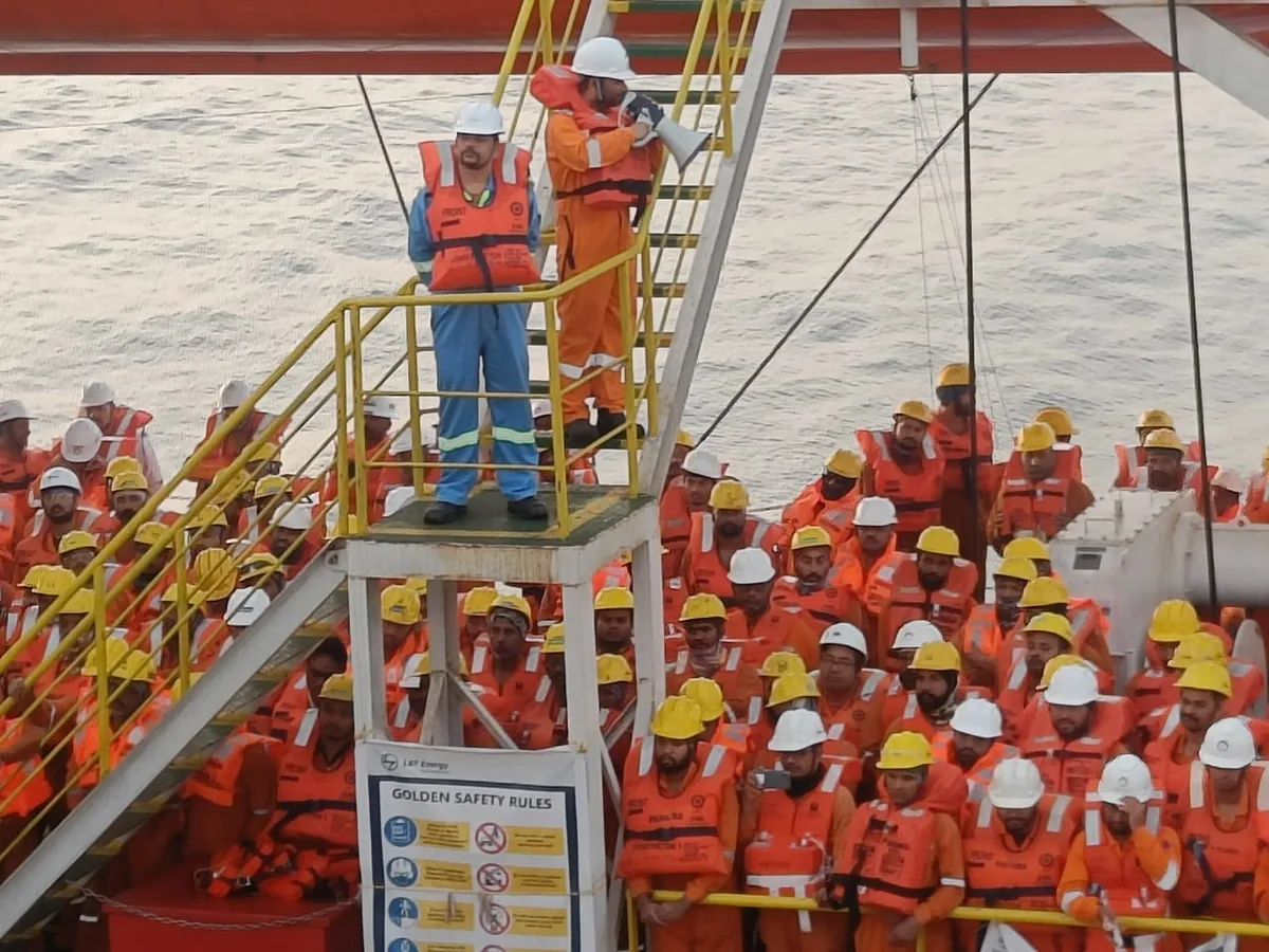Crew in orange lifejackets assemble beside a yellow stairway, with two personnel standing on the raised landing.