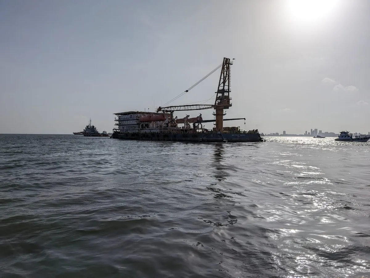 A crane vessel appears in silhouette on sunlit water, with smaller craft nearby.