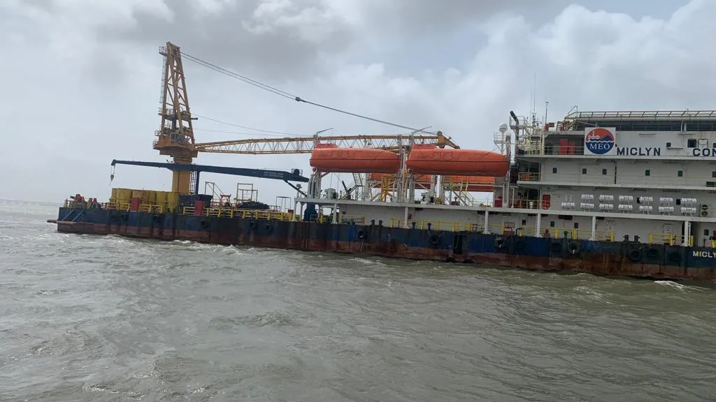The long working deck, lattice crane and orange lifeboats of an operational vessel extend across grey water.