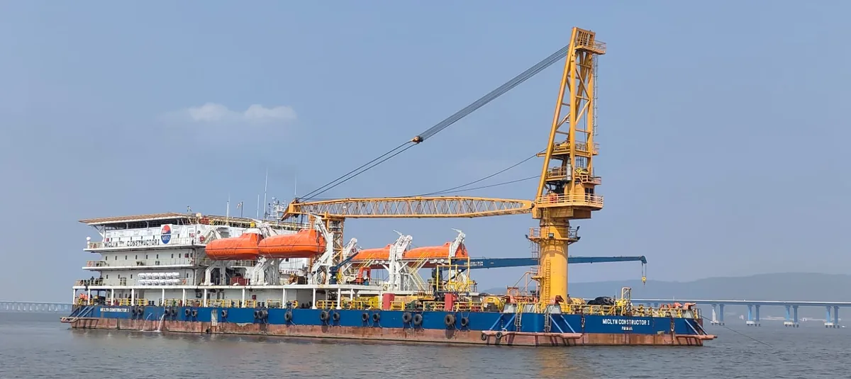 A full broadside view shows a crane vessel with a tall yellow crane and orange lifeboats near a distant bridge.