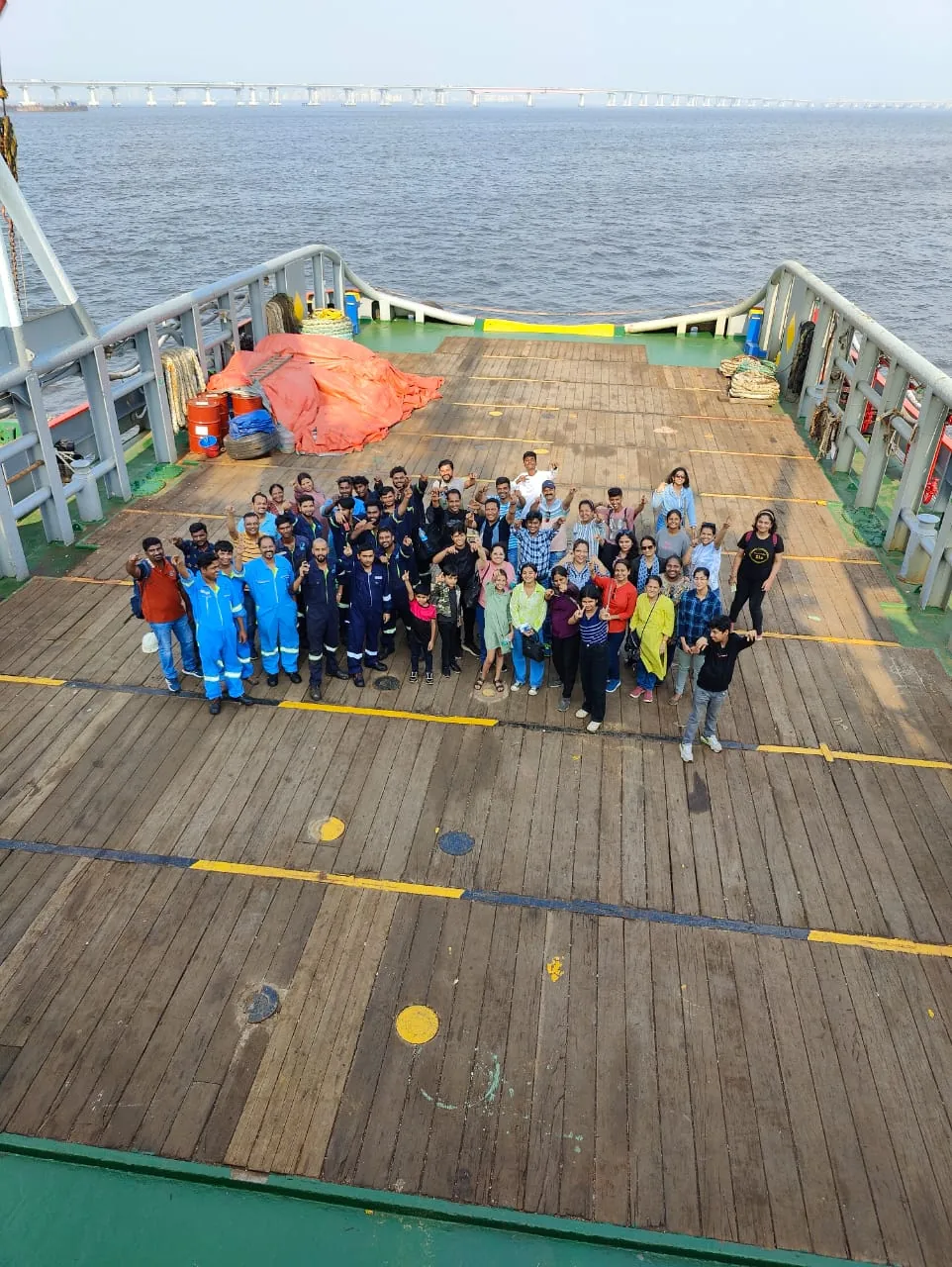 A group of personnel poses on an open vessel deck, with the sea stretching beyond the bow.