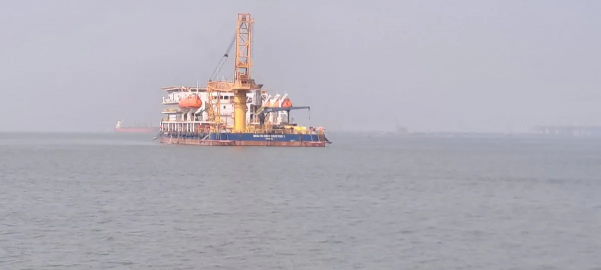 A distant crane vessel with a white accommodation block is seen through haze across open water.