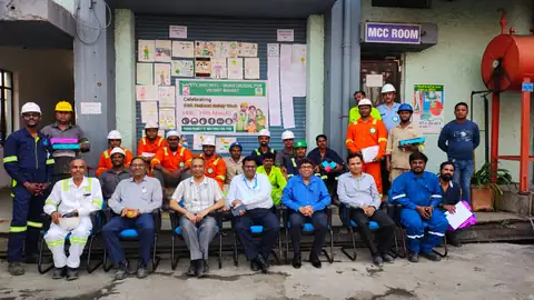 Terminal personnel in workwear and hard hats pose together outside an industrial facility during a safety gathering.