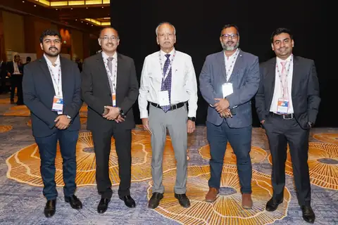 Five delegates stand together for a full-length group photograph in the conference hall.