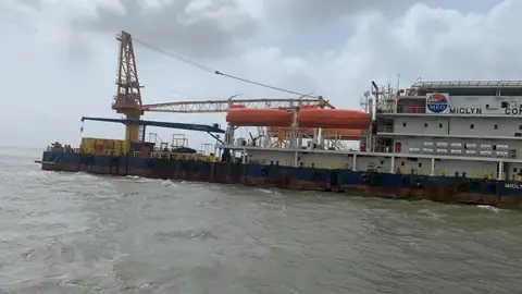 The long working deck, lattice crane and orange lifeboats of an operational vessel extend across grey water.