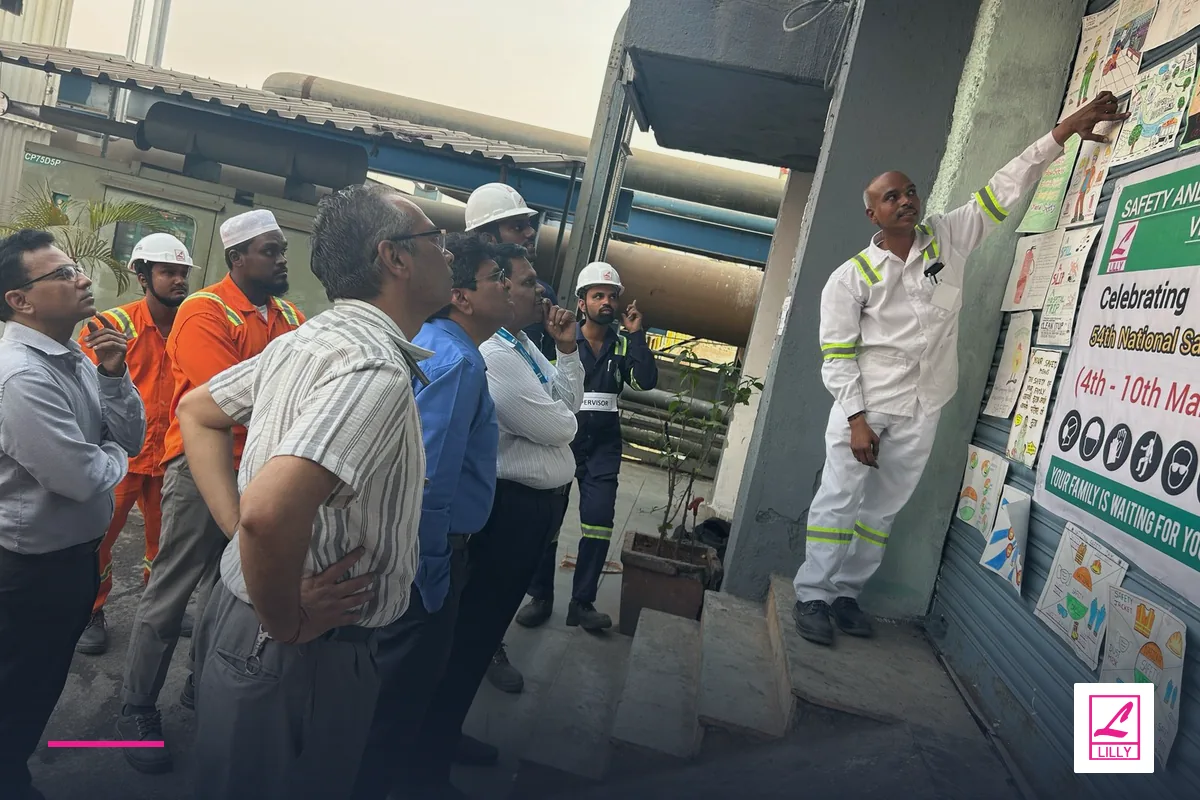 Terminal personnel attend a safety briefing beside industrial pipework, with a navy and magenta Lilly Maritime treatment.